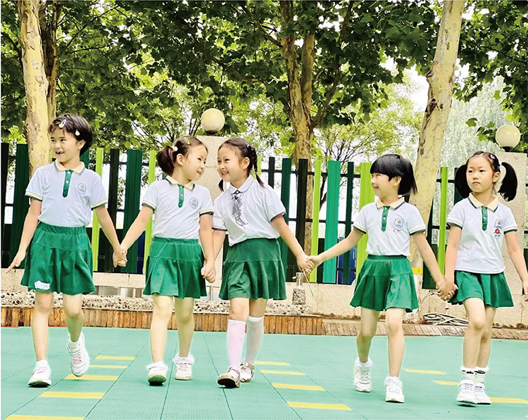 北部新区实验幼儿园女孩们身着绿白园服户外手拉手围圈的活动照片，校园特色