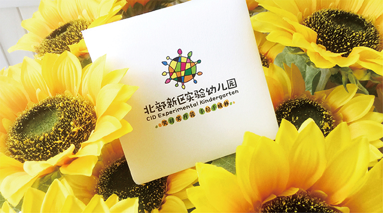 北部新区实验幼儿园物料样机，园徽卡片置于葵花花丛，教育品牌VI设计
