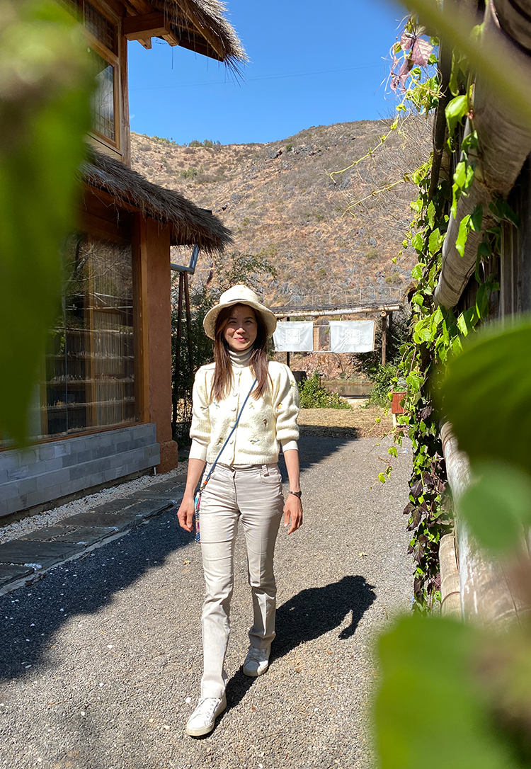 自然艺术家高意静戴帽行走于乡村石板路，背景青山与民居，锦连环2021文化之旅探访