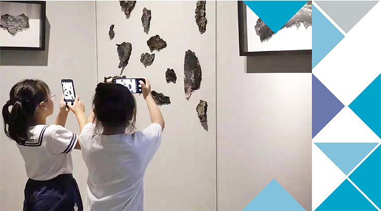 两名学生用手机拍摄墙上纸艺作品，锦连环锦学苑纸艺展校园文化场景