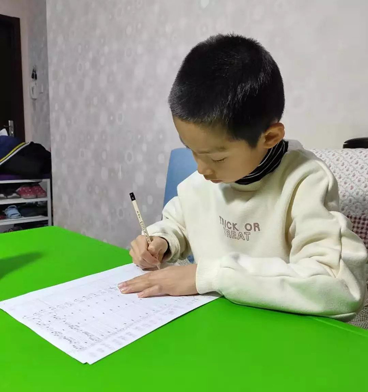 红英小学一名学生在家伏案手写抗疫进行曲乐谱，疫情期间居家创作场景