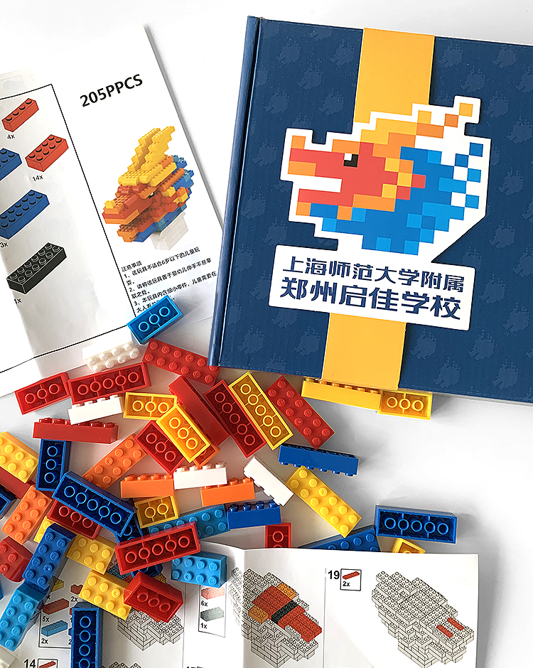 上师大附属郑州启佳学校VI品牌物料，印有像素龙校徽的笔记本搭配彩色积木，展现教育品牌设计应用
