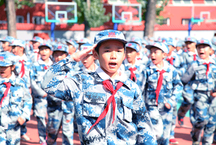 育鹰小学学生身着迷彩服在操场上敬礼，国防教育特色活动场景