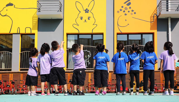 红英小学学生在黄色校园墙前排队,兔子小鹿墙绘环绕,阳光岛校园环境建设