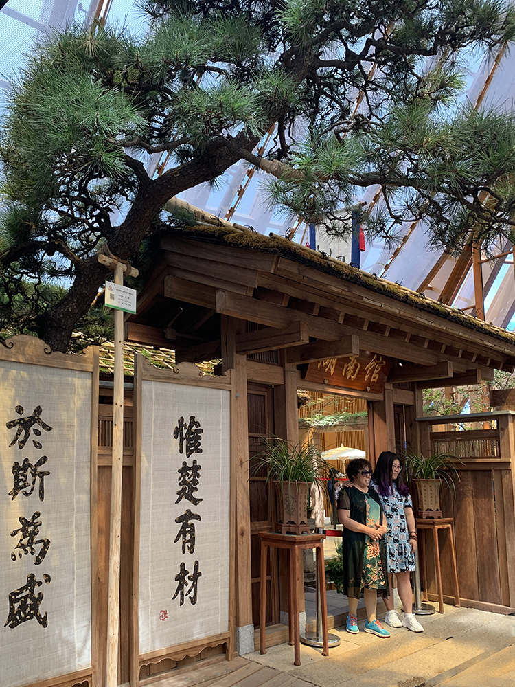 世园会湖南展园传统门楼,古松掩映,门柱悬惟楚有材楹联,游客驻足观赏