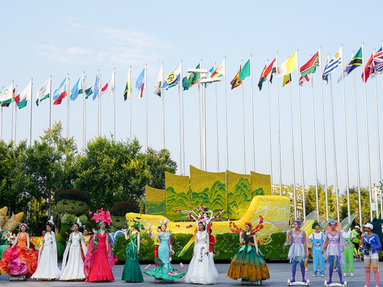 世园会国际区各国旗帜列阵,身着彩色民族服饰的人群在花卉景墙前合影