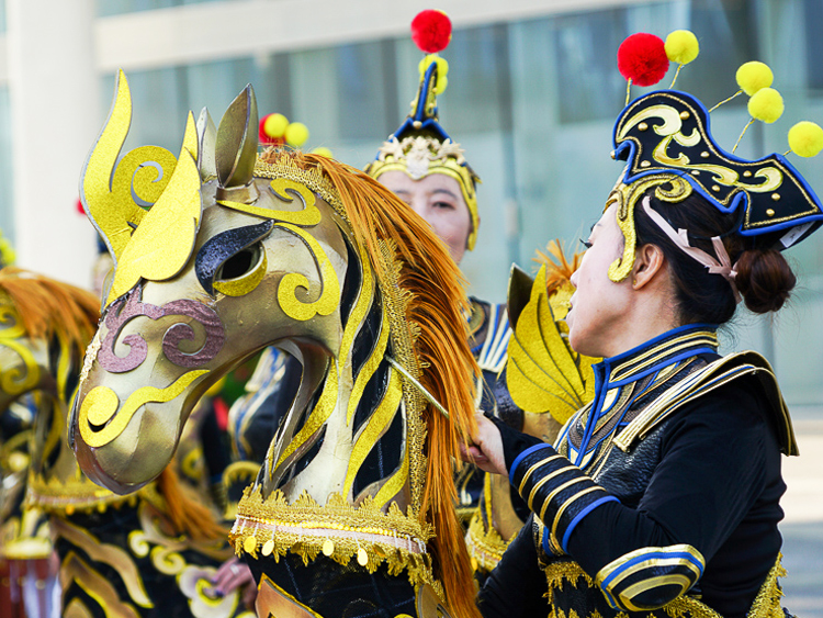 世园会巡游演出,演员佩戴金色骏马造型头饰与华丽戏装,民俗表演热闹