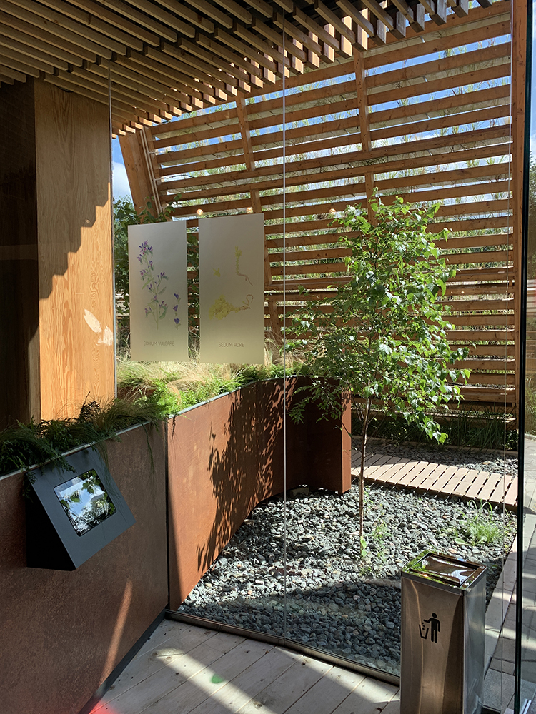 世园会展园木格栅庭院,绿树与卵石景观相映,展板讲述园艺主题,造景清雅