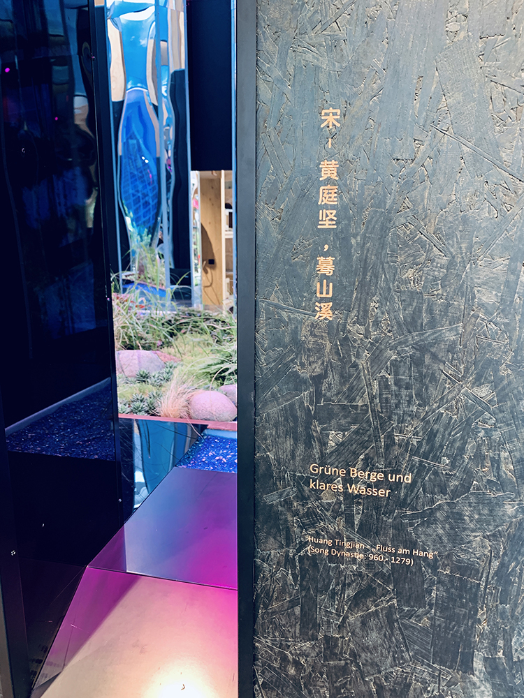 世园会深色展墙呈现宋代黄庭坚题刻图文,幽蓝水景映衬,展现植物文化底蕴