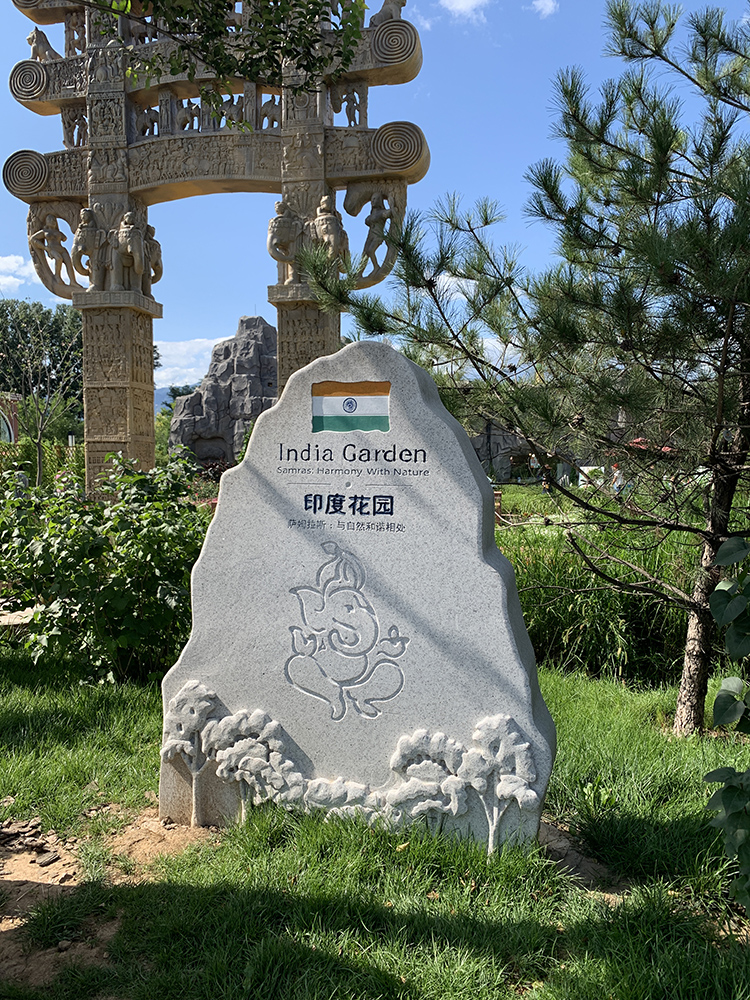 世园会印度花园入口景石,雕花石碑立于绿草间,标示展园身份
