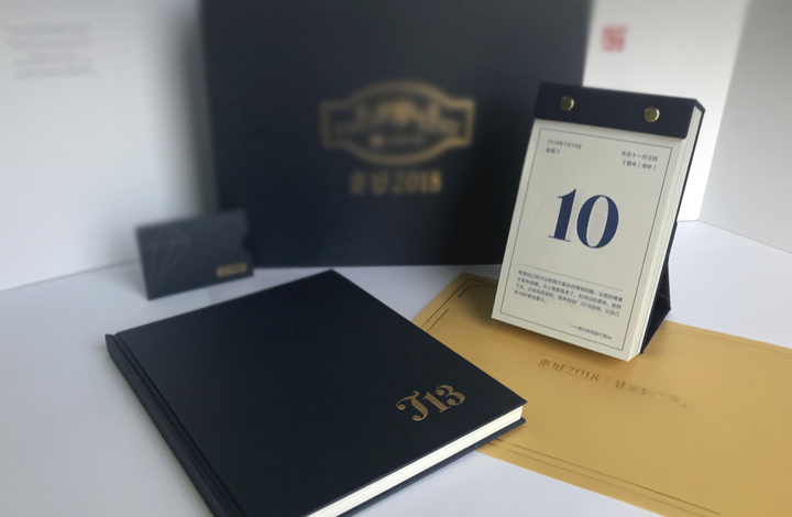 锦连环素雅系深色精装笔记本与桌面台历并置，封面烫金简约，尽显内涵厚重的品牌质感