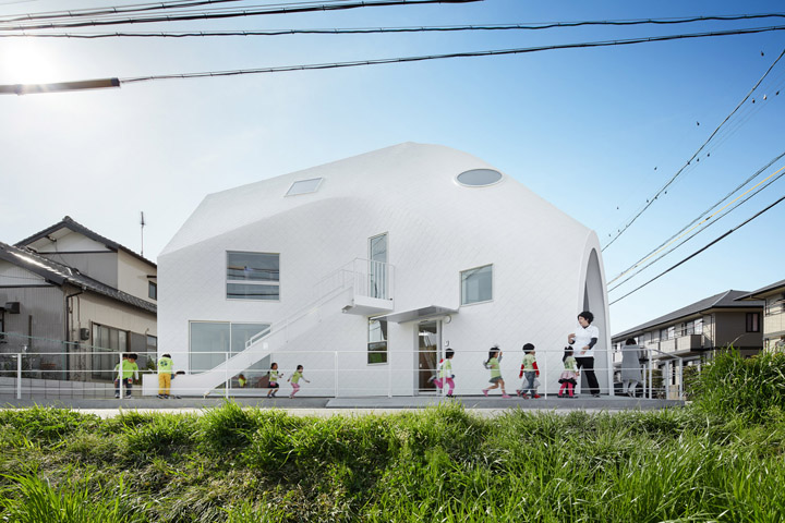 四叶草之家幼儿园白色沥青帐篷状建筑外景，孩子们在前方活动，体现幼儿园环境建设轻盈阳光的氛围