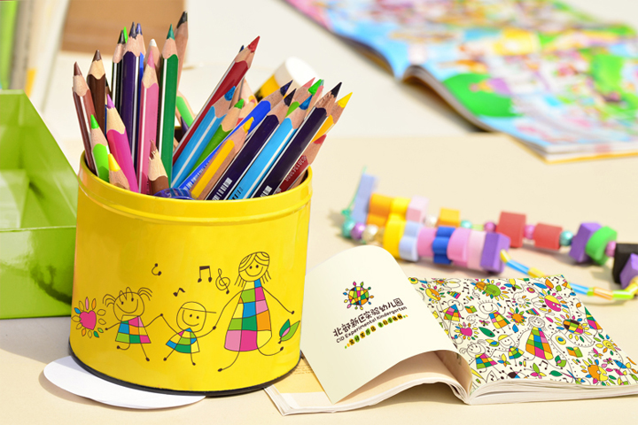 北部新区实验幼儿园文具用品VI应用，黄色笔筒印有儿童插画与园徽，搭配彩色铅笔与绘本，体现教育品牌设计