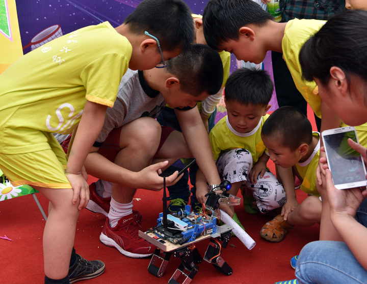 黄衣孩子们围观自制科技小车教师在旁指导，中科大幼儿园科学探索活动场景