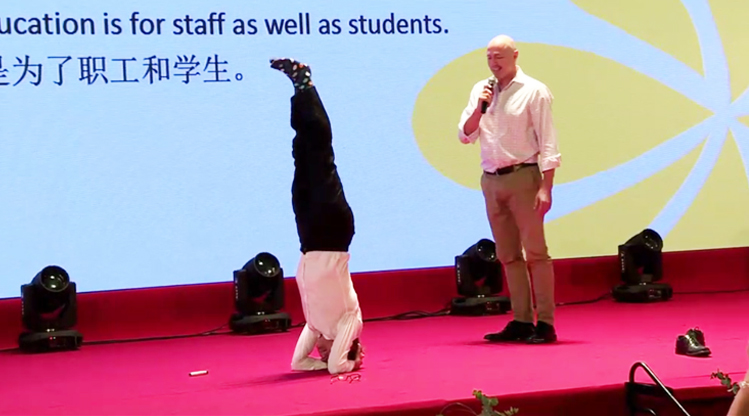 一位外籍嘉宾在大会舞台倒立演讲，大屏显示教育为了职工和学生