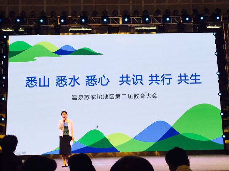 温泉苏家坨教育大会舞台，大屏呈现“悉山悉水悉心共识共行共生”主视觉，主持人登台