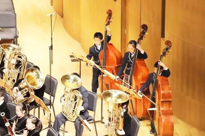 北京石油附小学生管乐团身着演出服合奏铜管与弦乐器，校园艺术教育现场