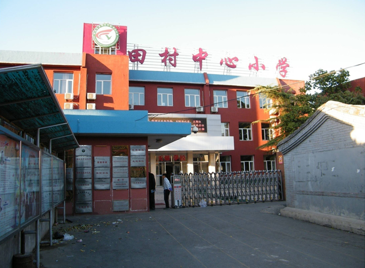 海淀区田村中心小学校门实景照片，红色教学楼前的校园入口环境面貌