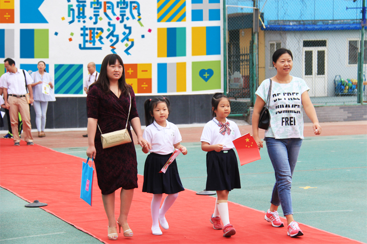 西二旗小学新生入校,教师带领戴红领巾女孩走过旗趣文化彩墙红毯,锦连环校园文化建设场景