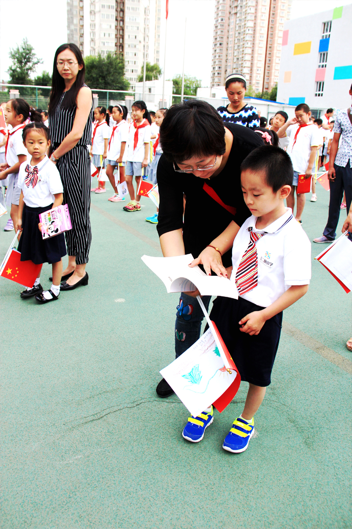 西二旗小学开学典礼,教师俯身帮助手持小红旗的新生男孩入场,锦连环旗趣文化校园活动现场