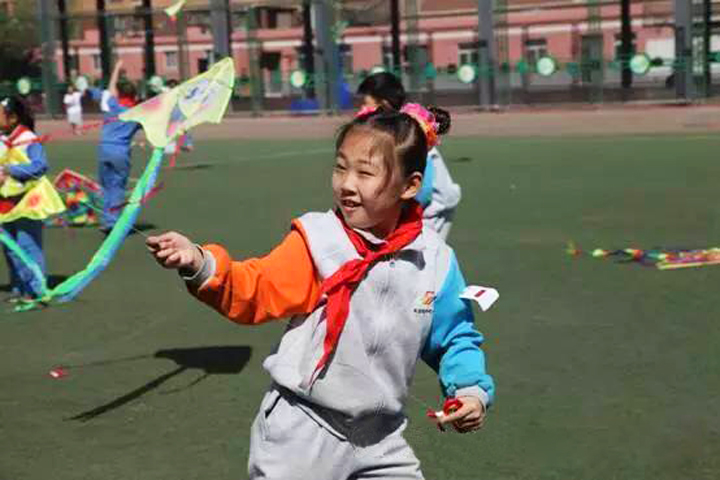 东北旺中心小学操场上戴红领巾女生奔跑放风筝，校园活力实景，特色定位成长体验