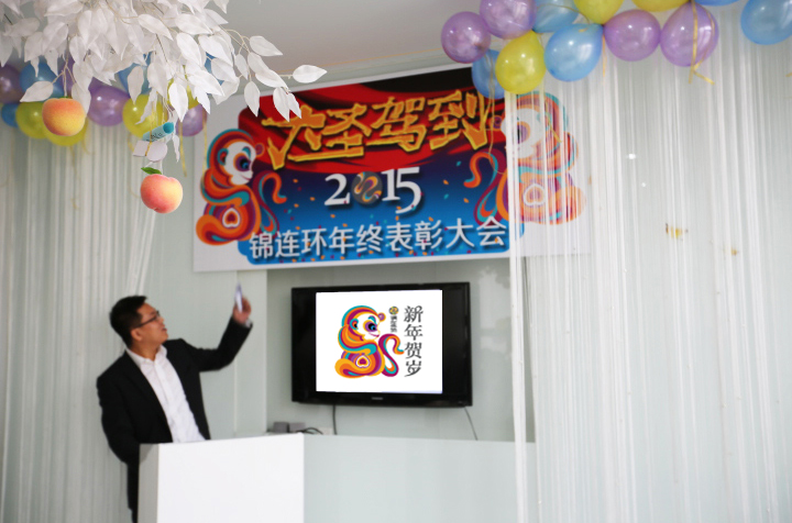 锦连环2015年终表彰大会现场，主持人站在写有年会主题的背景墙前发言