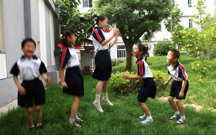 海淀区民族小学学生着校服在校园草坪活动，展现校服应用设计