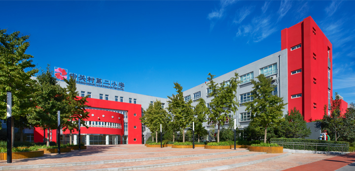 中关村第二小学红色教学楼外墙实景，蓝天下校徽墙与广场，锦连环校园建筑环境建设