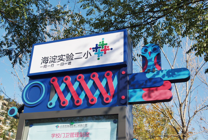 海淀实验二小校门口立体校牌与导视雕塑实景，红蓝弹簧造型体现校园导视系统设计